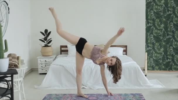 Gadis cantik muda berlatih yoga di rumah. Tidur di backgroud tersebut. sambil berpose berbeda sambil berdiri di atas tikar di kamarnya dengan pakaian olahraga yang indah — Stok Video