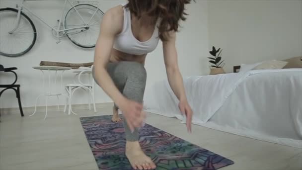 Hermosa joven está practicando yoga mientras hace ejercicios en la estera de su habitación. Primer plano. La cámara sigue los movimientos de las chicas — Vídeos de Stock