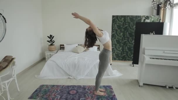 Mooi jong meisje oefent yoga oefeningen thuis. De camera van het algemene plan beweegt naar een close-up — Stockvideo