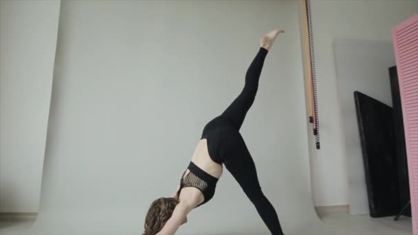 Jovem bonita pratica ioga enquanto faz asana em um fundo cinza em um sutiã de esportes preto e leggings pretos — Vídeo de Stock