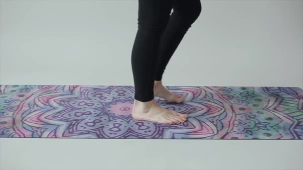 Een jonge vrouw loopt blootsvoets op een sport yoga mat. Close-up van de benen in zwarte legging. Langzame beweging — Stockvideo