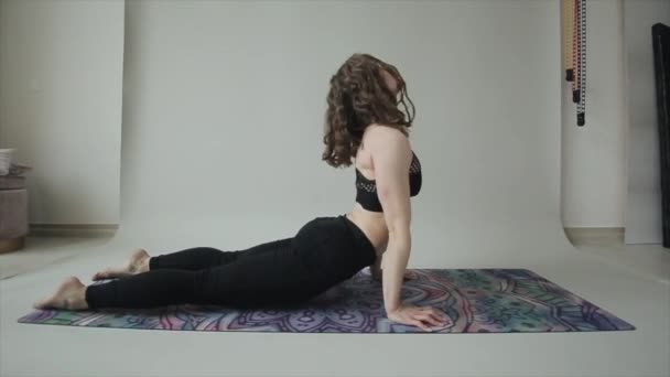 Молодая привлекательная девушка практикует йогу и делает различные упражнения дома. Камера движется вперед и вокруг девушки — стоковое видео
