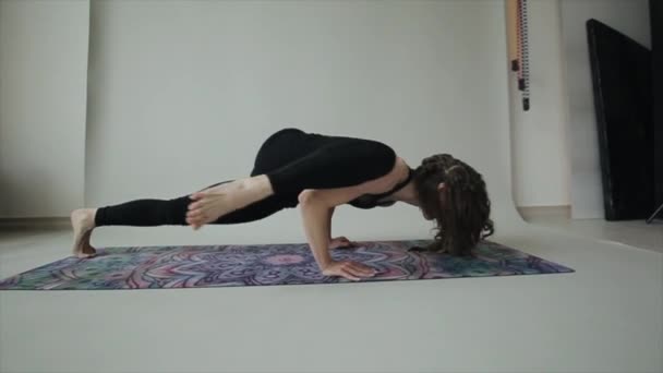 Молодая спортсменка практикует йогу дома делая упражнения один за другим стоя на коврике в спортивном лифчике и леггинсах — стоковое видео