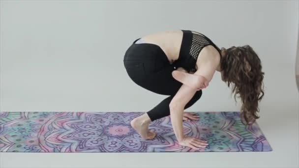 Young athletic girl practices yoga while doing complex exercises while standing on hands on a mat in black sportswear — Stock Video