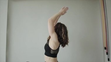 Güzel genç kız evde yoga yapıyor ve siyah spor kıyafetleri içinde bir minderin üzerinde dururken köprü pozu alıyor. Yakın plan.