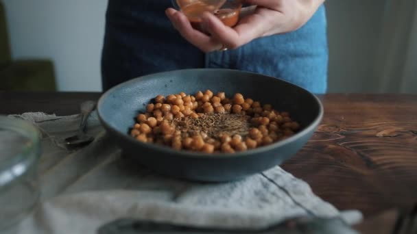 Een jong meisje neemt een lepel kruiden uit een blik en doet het in een kom met kikkererwten om hummus te bereiden. Close-up — Stockvideo