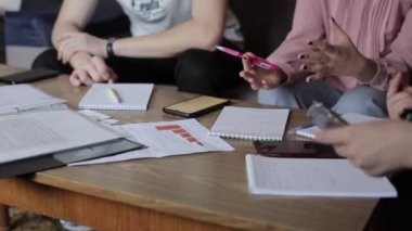 Gençlerin bir masada oturup iş konularını tartışarak not defterlerine not aldıkları bir iş toplantısına yakın çekim.