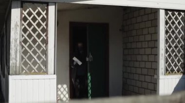 Bobruisk, Belarus - 20 Nisan 2020: Korunaklı uzun saçlı, koruyucu maskeli ve eldivenli genç bir kız, Coronavirus salgını sırasında ellerinde mektuplarla tuğla köy evinden çıkıyor.