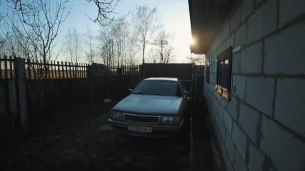 Bobruisk, Bělorusko - 20. dubna 2020: Zaparkované auto na nádvoří venkovského bílého cihlového domu proti slunné obloze. Ruská vesnice — Stock video