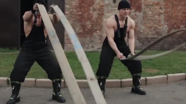 Twee gespierde jonge mannen trainen en doen crossfit oefeningen met gevechtstouwen. De camera beweegt achter de golven vandaan. Langzame beweging van de touwen — Stockvideo