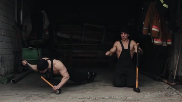 Dos hombres musculosos jóvenes entrenan y hacen flexiones basadas en grandes martillos y sonríen cuando el ejercicio falla. Primer plano — Vídeo de stock