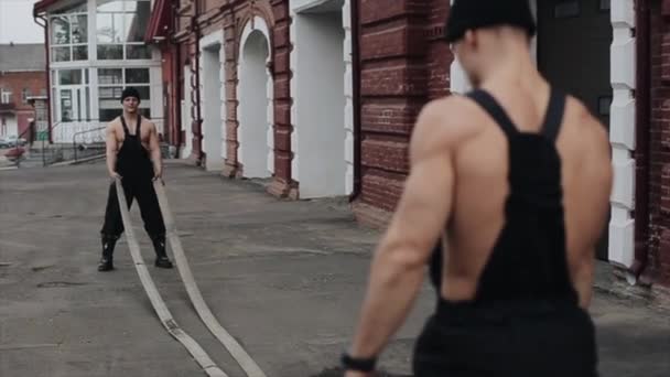 두 명의 젊은 근육질 남자가 훈련을 시키고 밧줄 과큰 망치로 운동을 한다. 크로스 핏. 뒷모습 — 비디오