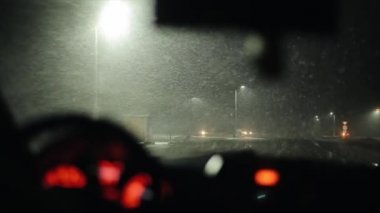 Karlı bir gecede, fenerlerle ve geçen arabalarla şehir yolunda bir arabanın ön camından bakmak. Ön planda bulanıklık. yavaş çekim