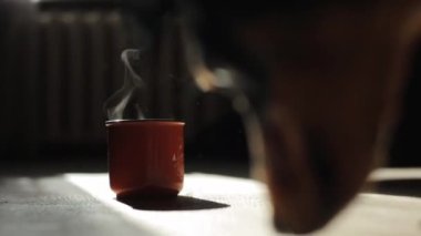 Odanın zemininde duran dumanı tüten bir çay bardağının yakın çekimi ve ön plandaki bir şeyi yalayan bir Dachshund köpeği.