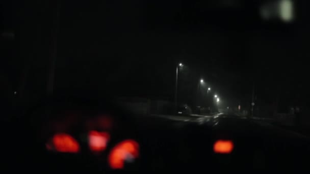 La macchina cavalca nella neve di notte su una strada della città. Vista attraverso il parabrezza di una macchina. Focus si sposta da sfondo a luci cruscotto — Video Stock