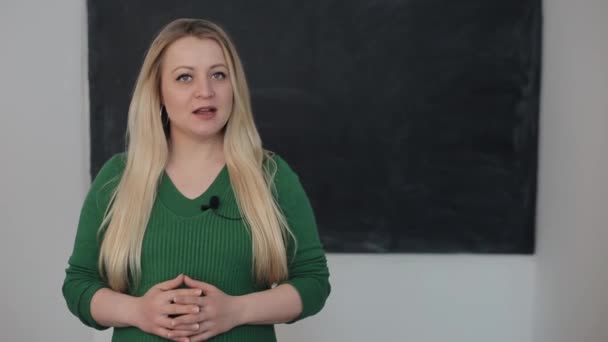 Jonge aantrekkelijke vrouw geeft les in de klas tegen de achtergrond van het schoolbord. Close-up — Stockvideo