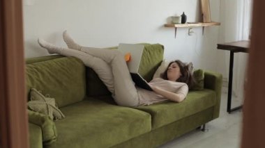 Genç serbest çalışan bir kız dizüstü bilgisayarla kanepeye uzanır ve onu tamamen kapatır ve odadan çıkar. Yakın plan.