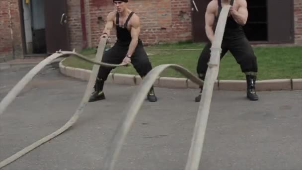 Twee aantrekkelijke gespierde jonge mannen trainen en voeren crossfit oefeningen uit met gevechtstouwen. De camera zoomt in close-up — Stockvideo