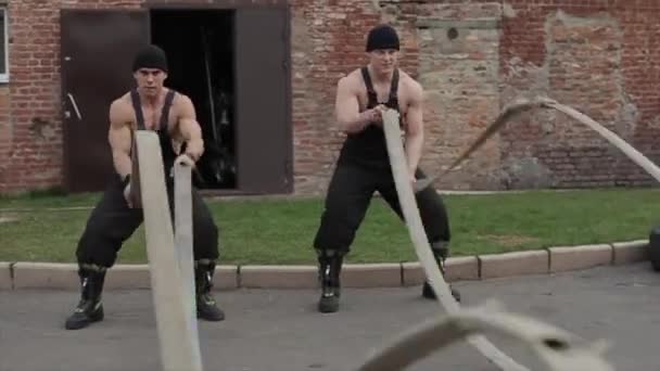Dos jóvenes musculosos entrenando y haciendo ejercicios de crossfit con cuerdas de batalla. La cámara se acerca de cerca — Vídeo de stock