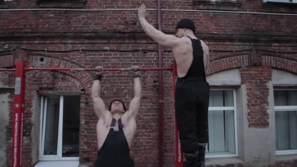 Twee jonge gespierde mannen ontspannen touwen voor cross-fit oefeningen tegen een rode bakstenen muur. Close-up. — Stockvideo