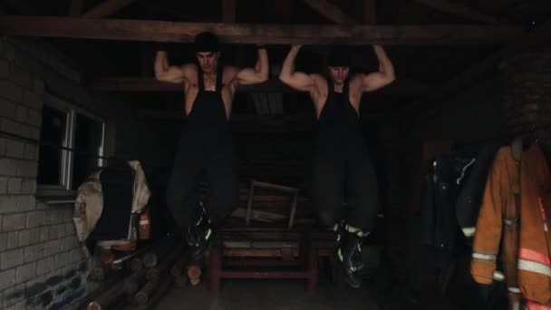Två unga muskulösa män tränar och drar upp på en träribba inomhus. Närbild. Kameran rör sig upp och ner — Stockvideo