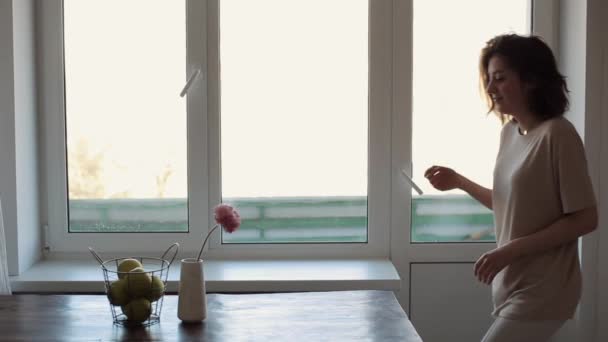 Una joven llega a la mesa en la que hay una cesta con manzanas y un jarrón con una flor toma una manzana y la vomita. Primer plano. Vista lateral — Vídeos de Stock