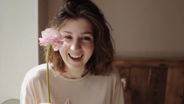A fiatal, gyönyörű, nevető lány virágot tart, és a szirmok szétmorzsolódnak az arcán. Közelkép — Stock videók