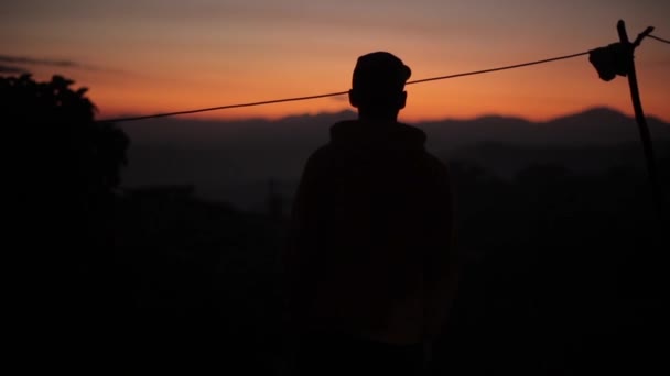 Een silhouet van een jonge man bij zonsondergang, zonsopgang in Azië, Nepal. Bergen, dorp. — Stockvideo