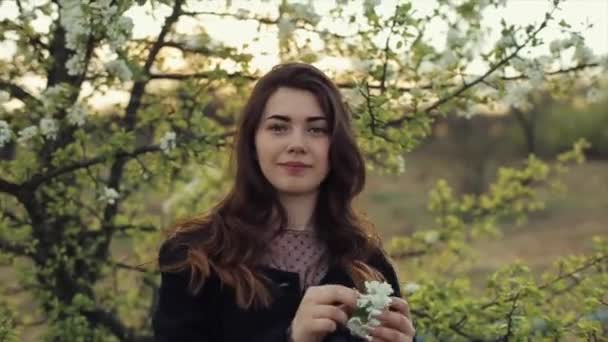 어느 아름다운 소녀는 꽃피는 정원에서 꽃피는 사과나무 가지로 머리를 장식하고 있는 산책을 즐긴다. 클로즈업 — 비디오