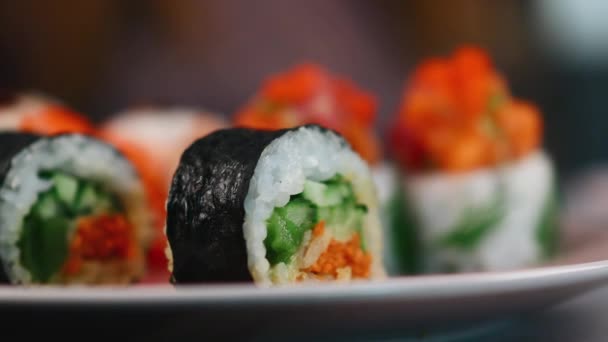 Rouleaux de sushi lumineux avec du poisson rouge et des légumes frais sur une assiette. Plat traditionnel japonais. Fusillade de macro. La caméra change de focus. 4K — Video