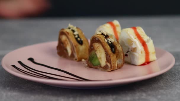 Rolos japoneses de sushi doce brilhante com várias frutas e creme de coalhada embrulhados em panquecas e encharcados com xarope e chocolate. Macro shot — Vídeo de Stock