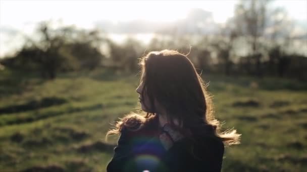 Ein charmantes junges Mädchen läuft durch den Park in den Strahlen der untergehenden Sonne glättet ihre Haare und lächelt süß. Nahaufnahme. Zeitlupe. Unklarer Hintergrund — Stockvideo
