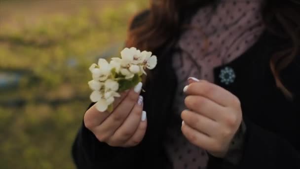 Una bella ragazza decora i capelli con un rametto di fiori mentre cammina in un giardino fiorito. Primo piano — Video Stock