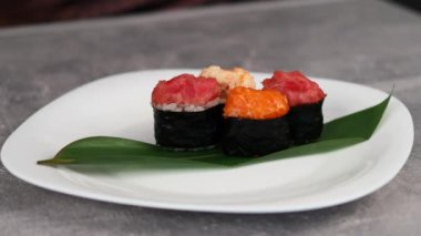 Genç bir kız, geleneksel suşi gunkan maki tabaklarına farklı dolguları ve nori yapraklarına sarılmış şekilde yayılıyor. Makro çekim