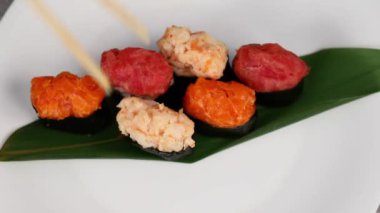Genç bir kız, oval suşi şeklindeki çeşitli dolgularla dolu bir Gunkan maki tabağı takıyor. Geleneksel Japon yemekleri. Makro atış. Yukarıdan bak. 4K