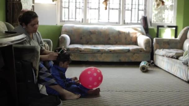 Κατμαντού, Νεπάλ - 27 Νοεμβρίου 2019: Μια Ινδή από το Νεπάλ κάθεται σε έναν καναπέ και χτενίζει ένα κοριτσάκι που κάθεται στο πάτωμα παίζοντας με ένα μπαλόνι. Κοντινό πλάνο — Αρχείο Βίντεο