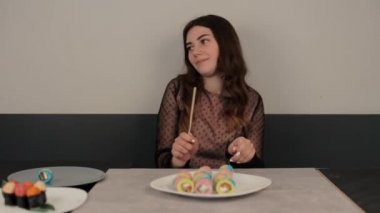 Neşeli bir kız bir kafede davul taklidi yaparak eğleniyor. Renkli suşi çubuklarını tabakta yuvarlar ve masada dans eder. Yakın plan.