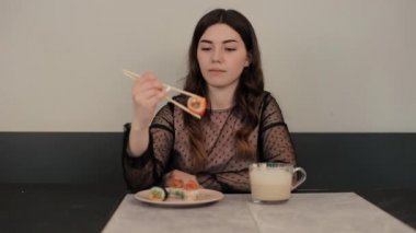 Geleneksel Japon mutfağı. Sevimli genç bir kadın büyük bir suşi böreği yiyor ve ağzı kapalı komik şişmiş yanaklarıyla gülüyor. Yakın plan.