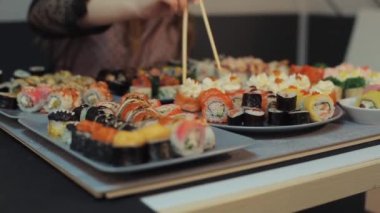 Kafkasyalı genç bir kız, bir sürü farklı rulonun olduğu bir masada oturan suşi barındaki rulolardan birini gösteriyor. Makro çekim