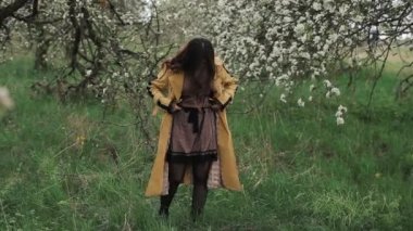 Romantik genç kız çiçek açan bahar bahçesinde çekim yapmadan önce kıyafetlerini ve saç stilini ayarlıyor. Yakın plan.
