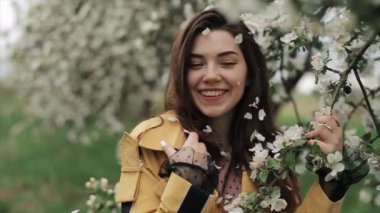 Çiçek açan ağaçların arasında yürürken saçlarında çiçek yaprakları olan neşeli genç bir kız. Bahar havası. Yakın plan. Yavaş çekim