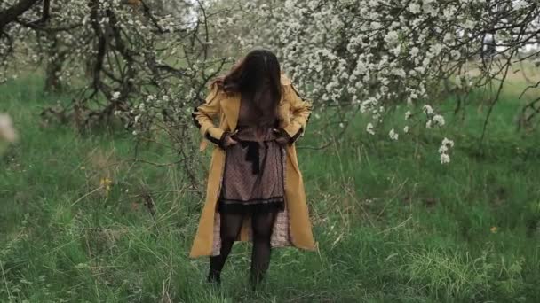 Romantico giovane ragazza regola i suoi vestiti e acconciatura prima di sparare nel giardino fiorito primavera. Primo piano — Video Stock