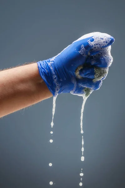 Мужская рука в голубой перчатке с капающей пеной — стоковое фото