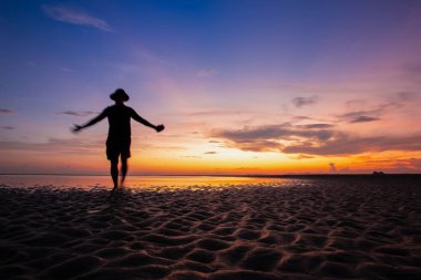 Gün batımında sahildeki siluet adam. Tatilde mutlu bir yaşam tarzı. Özgürlük hayatı. Renkli gökyüzü ve bulutlu manzara.