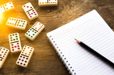 Not defteri ve kalemle birlikte çalışma masası. Tahta masada domino oyunu. Başarı için yönetim fikirleri. İş planlama kavramı.