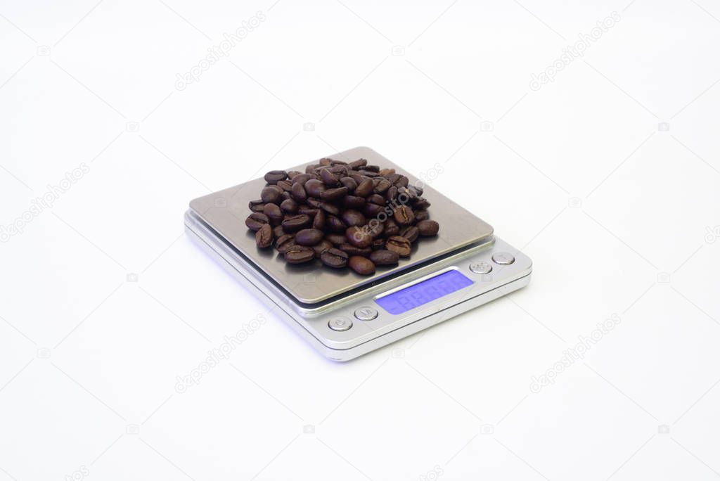 Dark roasted coffee beans on scales, close up.