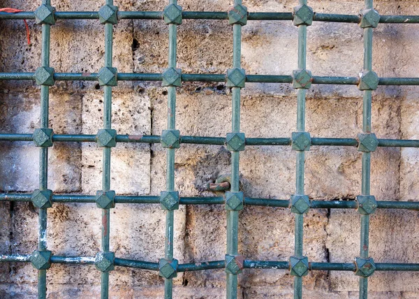 Uma velha parede de pedra atrás de uma grade de metal . — Fotografia de Stock