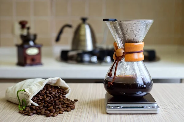 Coffee maker with filter and coffee beans in a bag on a wooden surface.