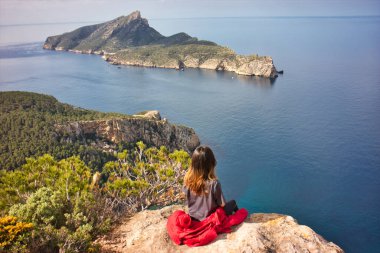 Gri spor elbiseli ve kırmızı kışlık ceketli hoş bir Asyalı kız Balear adalarındaki bu olağanüstü manzaranın tadını çıkarmak için dağa çıkıyor.