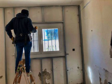 Adam merdivenlerde çalışıyor ve izolasyon ve alçıdan yeni bir ev yapıyor.